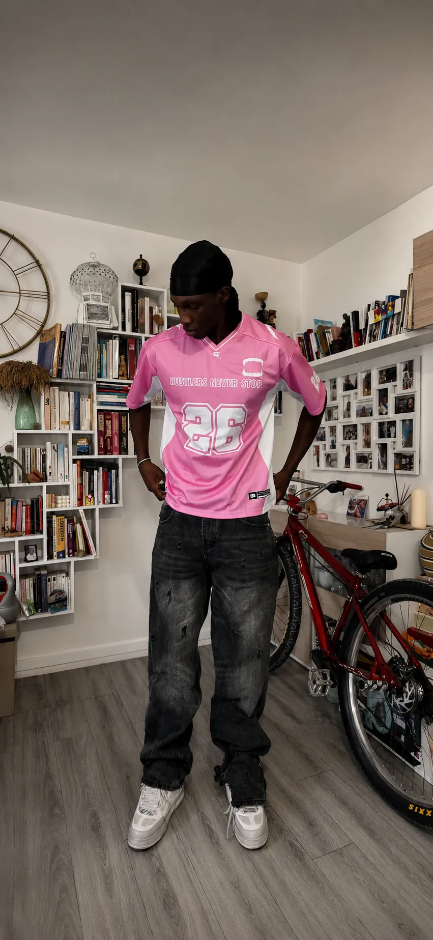 Rider GRINDZ en jersey FLAMINGO rose 26 devant un vélo et une bibliothèque