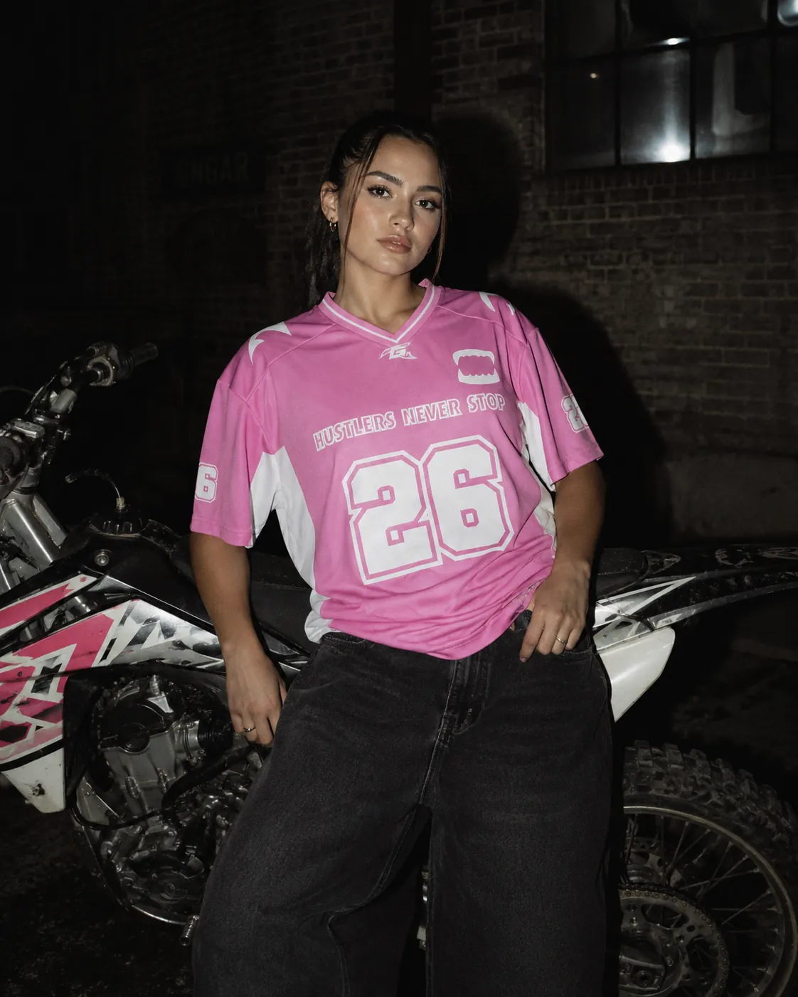 Rider GRINDZ en jersey FLAMINGO rose 26 appuyée contre une motocross