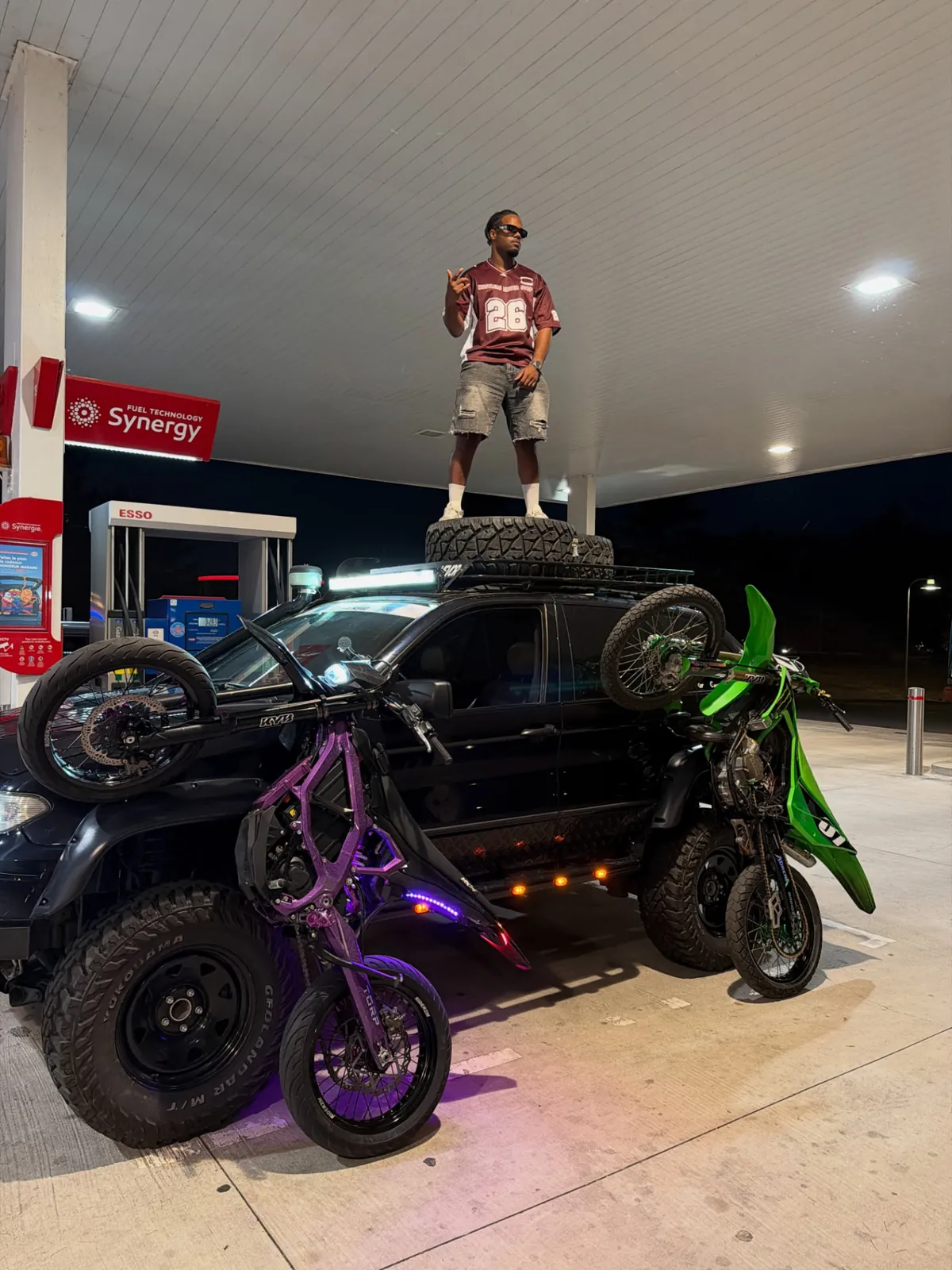 Rider GRINDZ en jersey 26 debout sur un 4x4 chargé de motocross en station-service de nuit